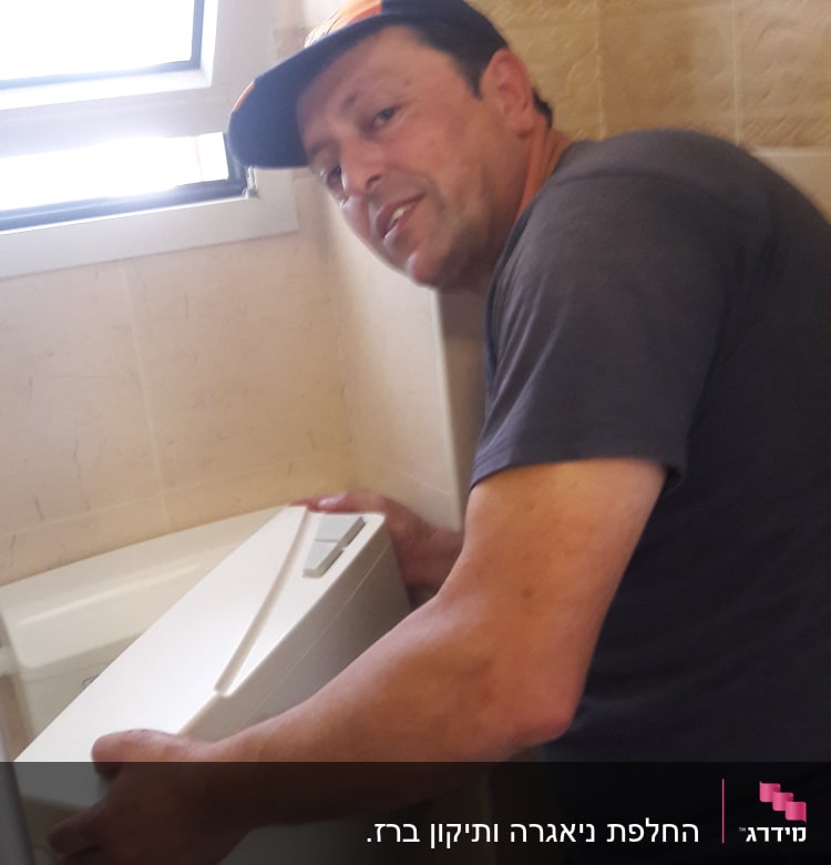 אדם מחזיק מכסה של מיכל הדחה בשירותים